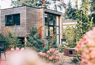 Een modern houten lodgehuis staat tussen bloeiende bloemen en groen in een rustige tuin vol planten.