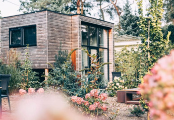 Et moderne træ-lodgehus omgivet af blomster og grønne planter i en smuk, frodig have om sommeren.