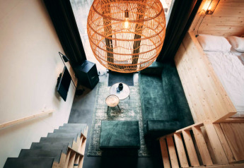 Intérieur de lodge moderne avec canapé vert, grande suspension en osier, lit et escalier en bois.
