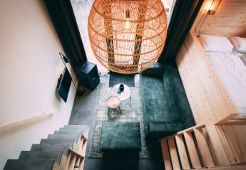 Interior de lodge moderno con sofá verde, escalera de madera, lámpara de mimbre y área de cama acogedora.