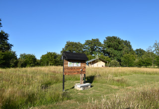 Informatiebord en tent in een grasveld op Camping Domaine Bleu Celeste in Auvergne-Rhône-Alpes, Frankrijk.