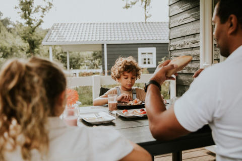 Familie frühstückt zusammen draußen an einem Tisch in der Forest Lodge, Camping Si-Es-An, Niederlande.