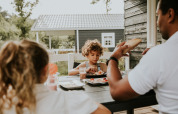 Familie frühstückt zusammen draußen an einem Tisch in der Forest Lodge, Camping Si-Es-An, Niederlande.