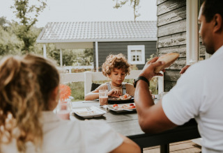 Famille prenant le petit-déjeuner dehors à une table à Forest Lodge, Camping Si-Es-An, aux Pays-Bas.
