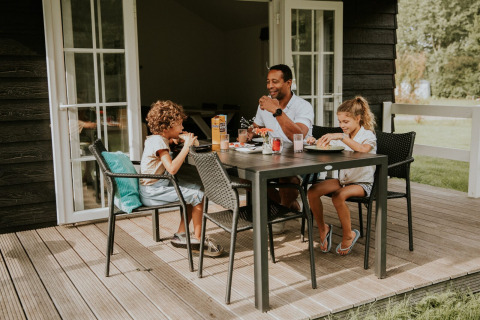 Gezin geniet van een maaltijd buiten op het terras bij Forest lodge, Camping Si-Es-An in Nederland.