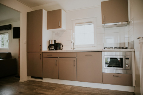 Moderne keuken in Forest Lodge op Camping Si-Es-An, Nederland, met oven, kookplaat en koffiezetapparaat.