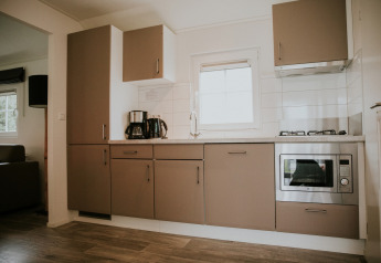 Moderne keuken in Forest Lodge op Camping Si-Es-An, Nederland, met oven, kookplaat en koffiezetapparaat.