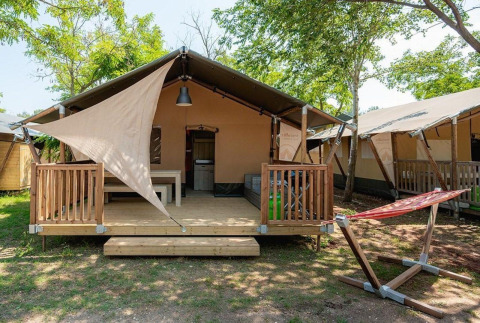 Vista del lodge Villatent Outback en Camping Au Clos de La Chaume, Francia, con terraza y hamaca exterior.