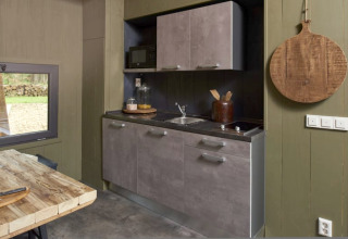 Modern compact lodge kitchen with gray cabinets, wood table, and round wooden board on olive wall.