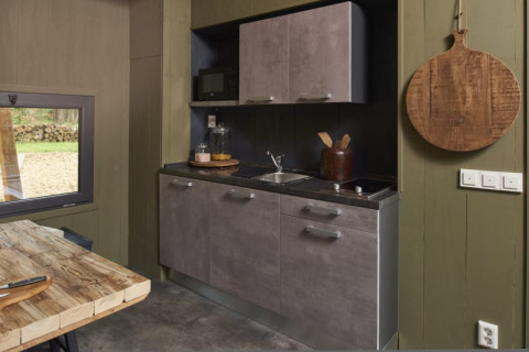 Moderne lodge-keuken met grijze kasten, houten tafel en een ronde houten plank aan een groene muur.