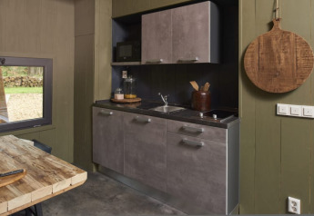 Piccola cucina moderna in un lodge con mobili grigi, tavolo di legno e tagliere rotondo appeso al muro.