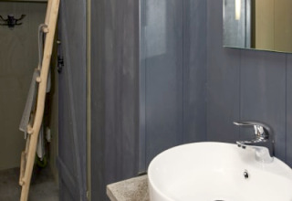 Modern lodge bathroom featuring a round white sink, dark blue walls, a mirror, and rustic wooden accents.