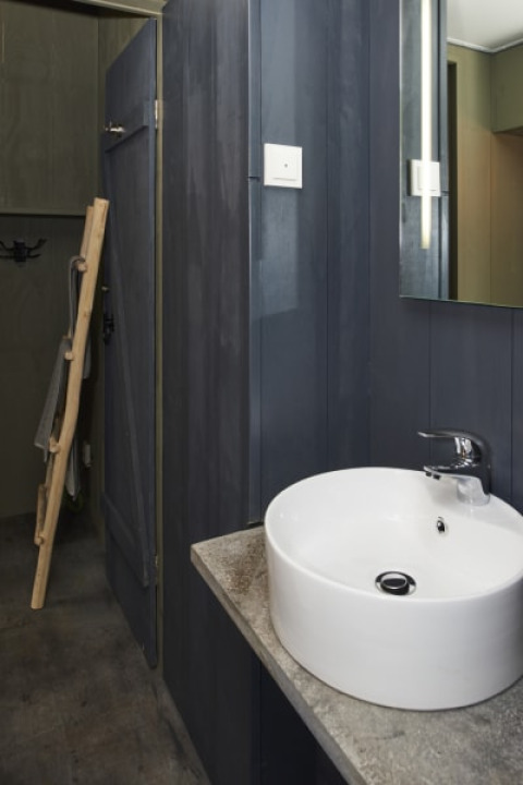 Baño moderno en una cabaña con lavabo redondo blanco, paredes oscuras y un espejo colgado en la pared.