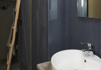 Baño moderno en una cabaña con lavabo redondo blanco, paredes oscuras y un espejo colgado en la pared.