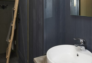 Baño moderno en una cabaña con lavabo redondo blanco, paredes oscuras y un espejo colgado en la pared.