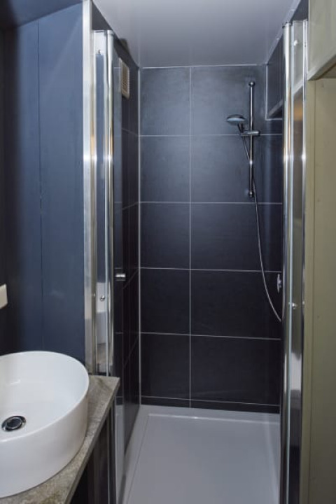 Baño moderno en una cabaña con ducha de azulejos negros, puerta de cristal y lavabo blanco redondo.