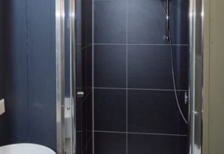 Baño moderno en una cabaña con ducha de azulejos negros, puerta de cristal y lavabo blanco redondo.