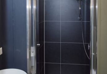 Baño moderno en una cabaña con ducha de azulejos negros, puerta de cristal y lavabo blanco redondo.