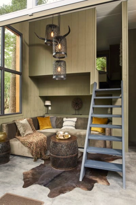 Cozy lodge interior with large windows, a sectional sofa, animal hide rug, and ladder to a loft space.
