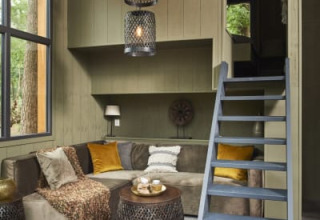 Gezellige lodge met hoekbank, groot raam, dierenvacht, salontafel en trap naar een knusse vide.