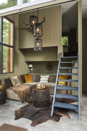 Cozy lodge interior with large windows, a sectional sofa, animal hide rug, and ladder to a loft space.