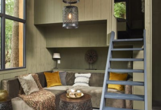 Cozy lodge interior with large windows, a sectional sofa, animal hide rug, and ladder to a loft space.