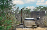 Bain nordique en bois et cabanes entourés de forêt près d’un lodge, sous un ciel bleu nuageux.