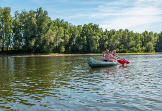 Deux personnes pagayant en canoë sur un lac paisible, à côté d'arbres, pour glamping dans un parc de vacances.