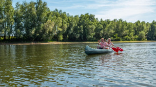Dos personas remando en una canoa sobre un lago tranquilo cerca de árboles, perfecto para glamping en parque.