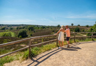Ein Paar genießt den Panoramablick von einem Zaun im Glamping-Urlaubspark an einem sonnigen Tag.