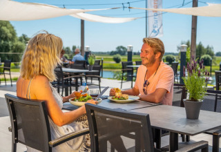 Et par nyder frokost udendørs på en restaurant ved vandet i en feriepark med glamping faciliteter.