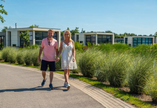 Couple marchant main dans la main dans un parc de vacances avec des lodges glamping modernes et de la verdure.