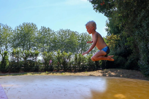 Een kind in zwembroek springt op een groot luchtkussen in een zonnig glamping vakantiepark.