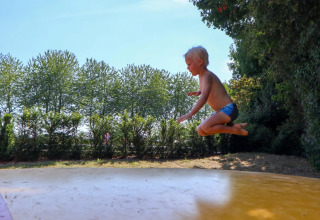 Et barn i badebukser hopper på en stor oppustelig pude i en solrig glamping-feriepark.