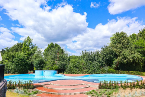 Piscina exterior con escalones y jardín frondoso en un glamping en parque vacacional bajo cielo azul.