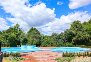 Udendørs swimmingpool med trapper og frodig have baggrund ved glamping feriepark under blå himmel.