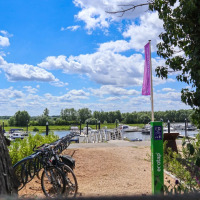 Bicicletas aparcadas junto a un río con barcos y muelle, cielo soleado y naturaleza en parque vacacional.