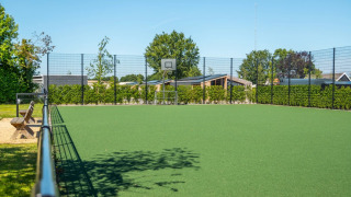 Campo deportivo multiusos con canasta de baloncesto en parque vacacional, rodeado de cabañas y vegetación.
