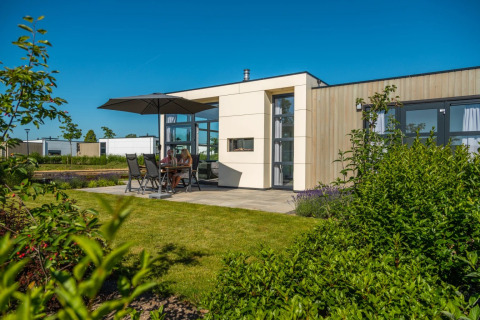 Cabaña glamping moderna con jardín, terraza y sombrilla en un parque vacacional bajo un cielo azul claro.