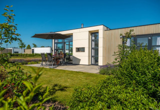 Cabane de glamping moderne avec jardin, terrasse et parasol dans un village vacances sous ciel bleu.