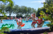 Kinderen spelen en zwemmen in een openluchtzwembad op een vakantiepark met glamping, omringd door bomen.