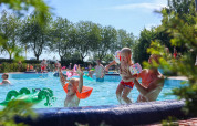 Des enfants s'amusent et nagent dans une piscine extérieure d’un parc de vacances avec glamping, entouré d’arbres.