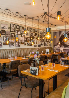 Restaurante moderno con pared decorada con fotos en blanco y negro, luces cálidas y asientos confortables.