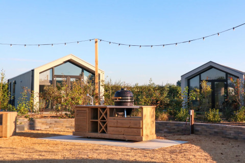 Moderne Glamping-Hütten in einem Ferienpark mit Außenküche und Lichterketten im Sommerlicht.