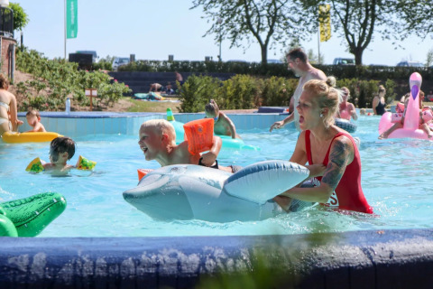Lifeguard assists a child with an inflatable dolphin in a swimming pool at a sunny holiday park.