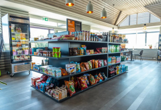 Moderne butik i et feriepark glampingområde med snacks, drikkevarer og siddepladser i solen.