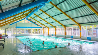 Overdekt zwembad met badgasten in een vakantiepark, grote ramen met uitzicht op de buitenomgeving.