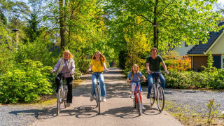 Een vrolijk gezin fietst samen op een zonnige dag in een groen vakantiepark met glamping accommodatie.