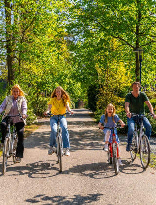 Una familia feliz anda en bicicleta junta en un día soleado en un parque vacacional verde con glamping.