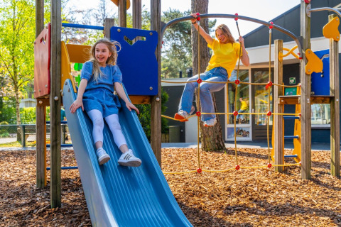 Twee meisjes spelen op een glijbaan en klimnet op een speeltuin bij een vakantiepark met glamping.